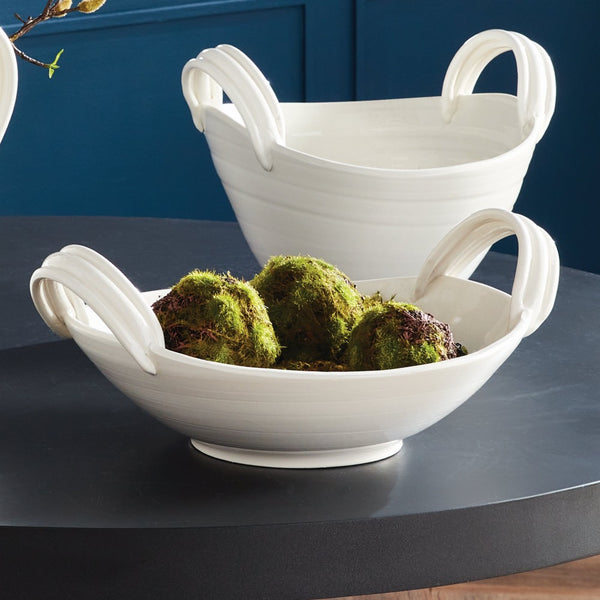 White ceramic bowl with handles filled with green moss on a dark surface.