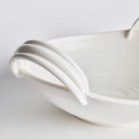 Close-up of a white ceramic bowl with a white handle on a light gray background