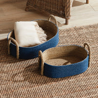 Two woven baskets with handles on a textured rug