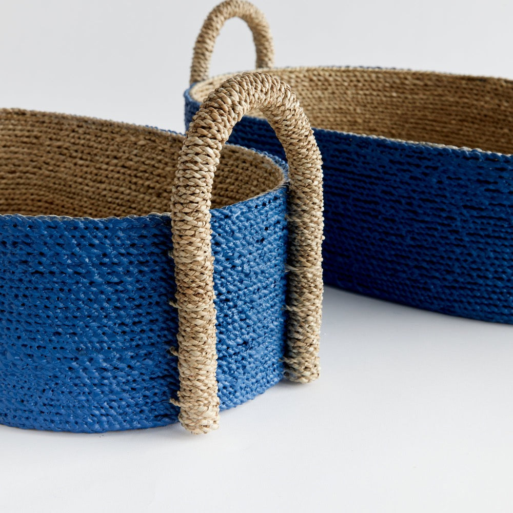 Two woven baskets, blue and natural seagrass, with handles on a light gray background.