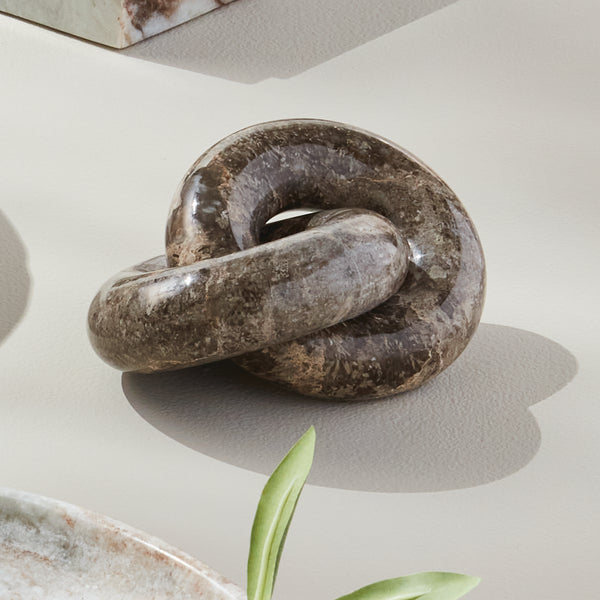 Marble knot sculpture on a light surface with a plant in the corner