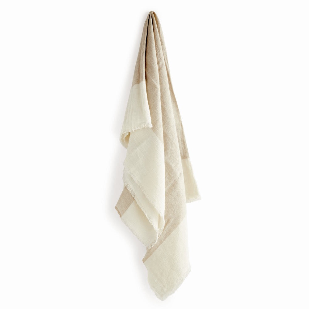 A lightweight woven throw blanket in a soft beige and cream color-blocked pattern, hanging against a plain white background.