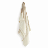 A lightweight woven throw blanket in a soft beige and cream color-blocked pattern, hanging against a plain white background.