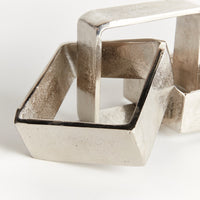 The Corbin Square Chain Sculpture by Napa Home & Garden features two oversized, interlocked metallic chain links.