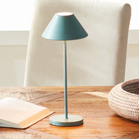 Table lamp with a teal shade on a wooden surface next to an open book and woven basket.