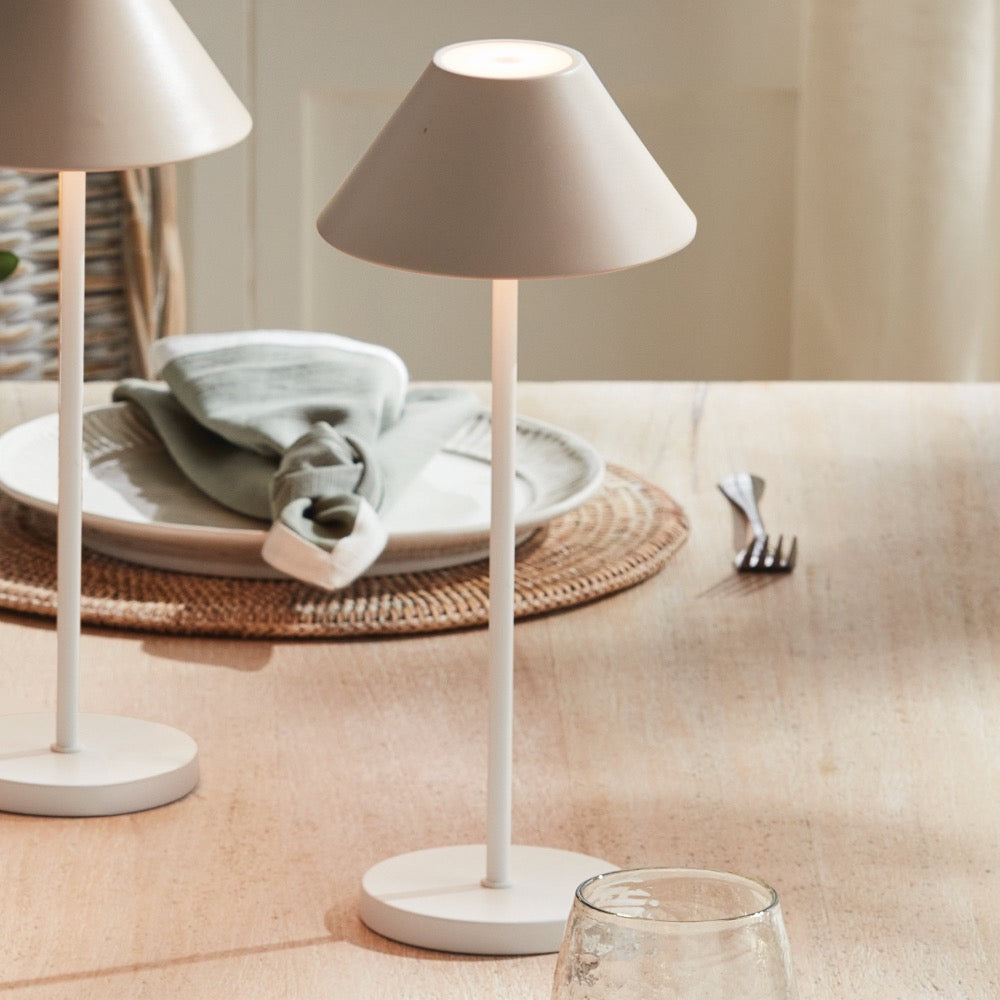 Beige table lamp on a beige surface with a plate and cutlery in the background