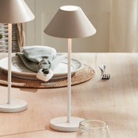 Beige table lamp on a beige surface with a plate and cutlery in the background