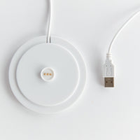 White wireless charging pad with USB cable on a light gray background