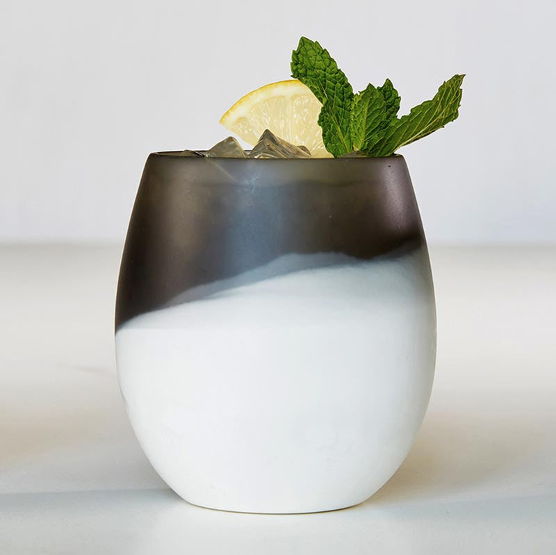A Santa Barbara Design Studio resin two tone stemless wine glass with ice, lemon slice, and mint leaves.