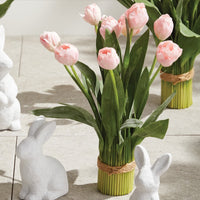 Bouquet of pink tulips in a green vase with two white ceramic bunnies on a wooden surface.