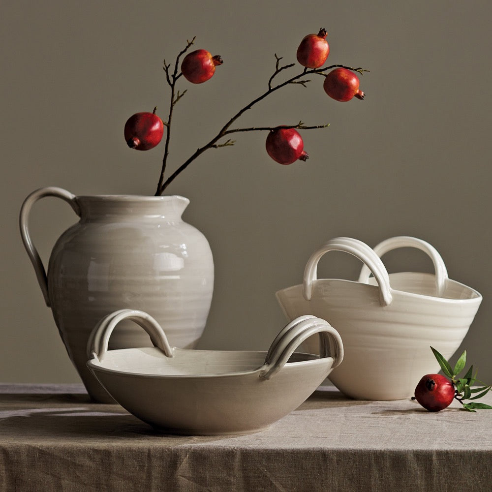 Set of ceramic bowls and a pitcher with red pomegranates on a neutral background