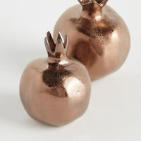Two bronze-colored decorative items resembling pomegranates on a light gray background