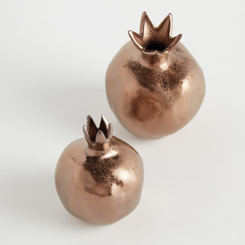 Two copper-colored decorative items shaped like pomegranates on a light gray background