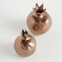 Two copper-colored decorative items shaped like pomegranates on a light gray background