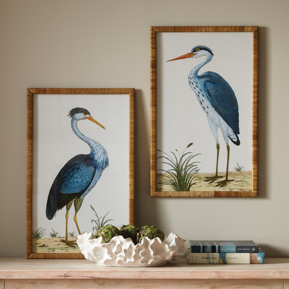 Two framed prints of herons on a wall above a wooden surface with decorative items.