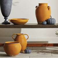 Decorative ceramic vases and bowls on a wooden shelf with pumpkins.