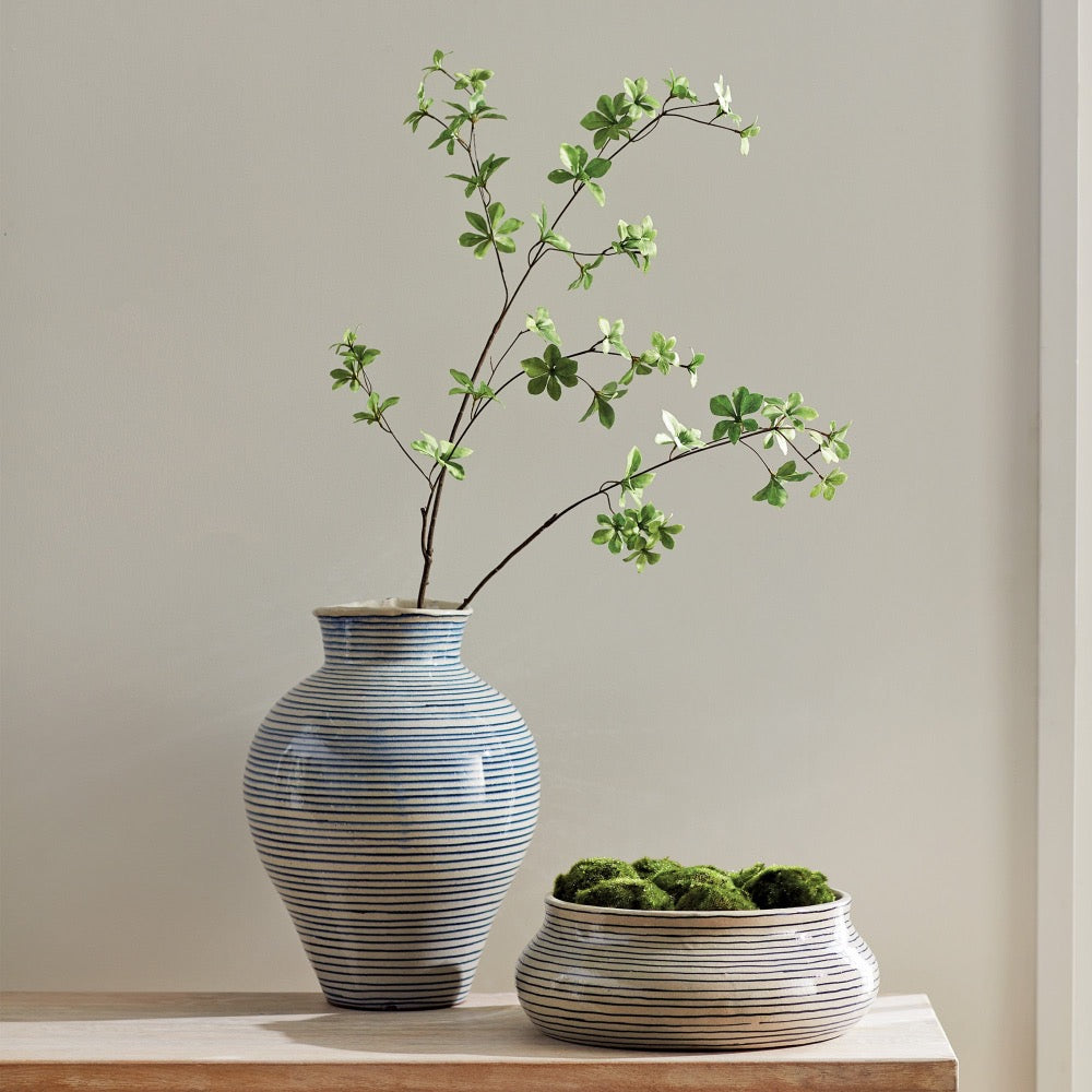 Two ceramic vases with striped patterns and greenery on a neutral background