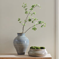 Two ceramic vases with striped patterns and greenery on a neutral background