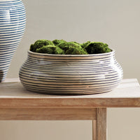 Ceramic planter with striped design filled with green moss on a wooden surface.
