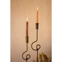 Two lit taper candles in dark metal scroll candlesticks against a warm beige background.
