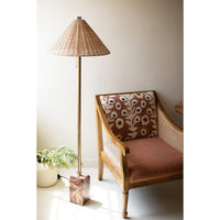 Chair with floral pattern and woven armrests next to a floor lamp with wicker shade in a room.