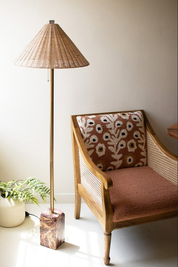 Chair with floral pattern and woven armrests next to a floor lamp with wicker shade in a room.