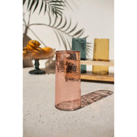 Pink glass vase on a textured surface with decorative elements in the background
