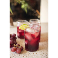 Red cocktails with ice and lemon slices in glasses on a stone surface, accompanied by grapes.