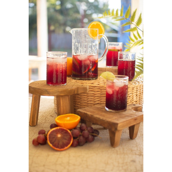 Glass pitchers and glasses of red punch on a wooden table outdoors.