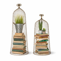 Two decorative wired mesh cloche topiaries with books and plants on a white background