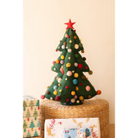 Green felt christmas tree with colored pom pom balls on a rattan riser and wrapped presents on a beige background.