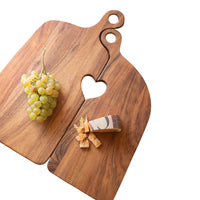 Wooden cutting board with heart-shaped hole, grapes, and cheese on a white background