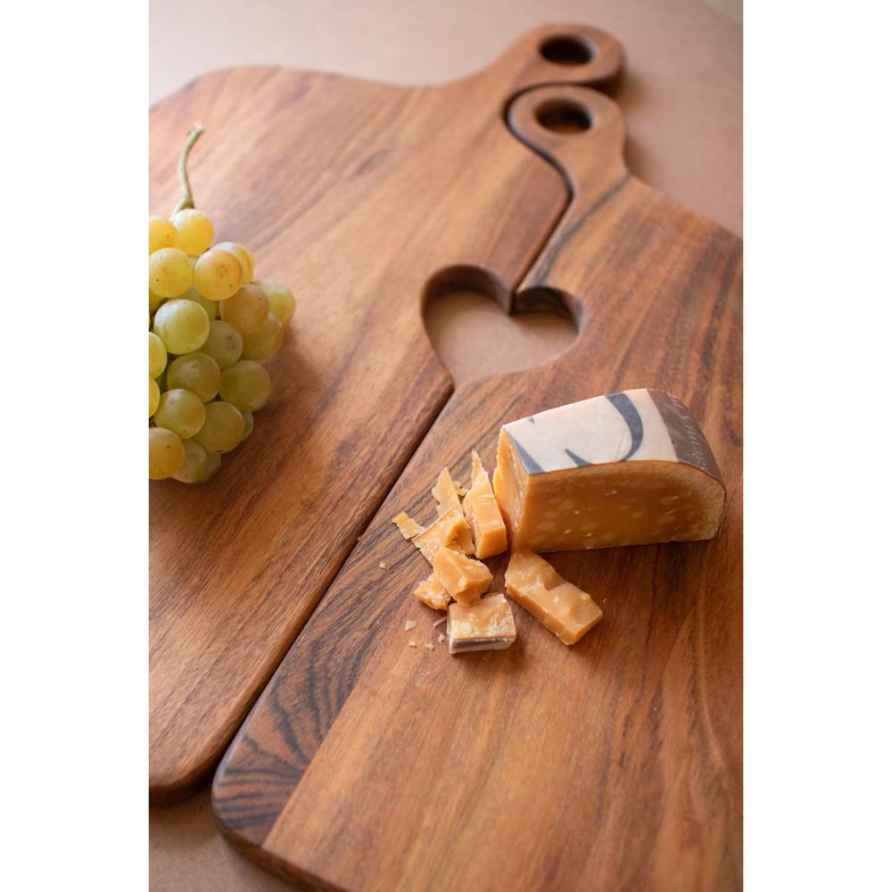 Wooden cutting board with heart-shaped handle, grapes, and cheese on a light background