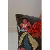 Close-up of a dark brown velvet throw pillow featuring colorful hand-embroidered floral and textured botanical motifs in red, beige, blue, and gray.