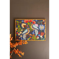 Framed artwork with colorful birds and flowers on a dark wall.