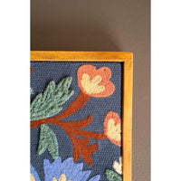 Floral embroidered design on fabric with wooden frame against a dark background