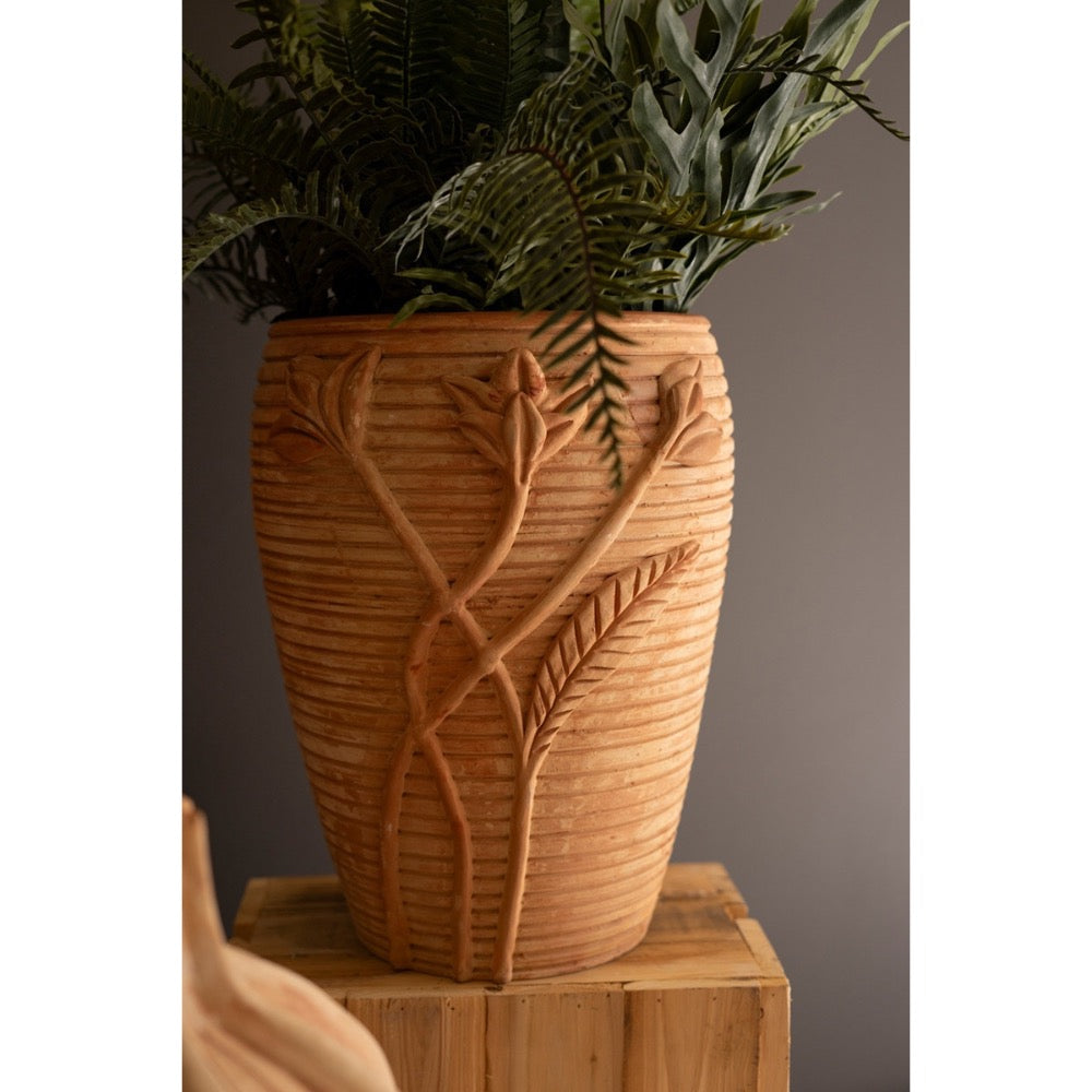 Decorative terracotta vase with plant on a wooden surface against a neutral background