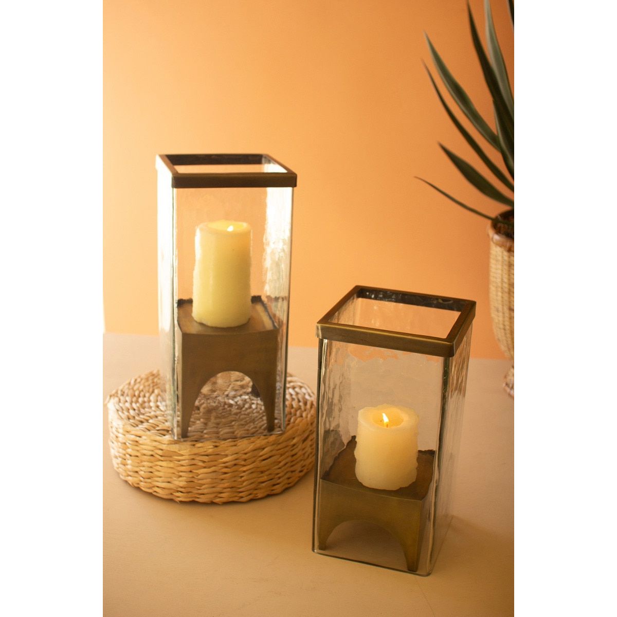 Two glass candle holders with candles on a surface against an orange wall.