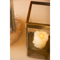 Candle in a glass lantern with a brass frame on a reflective surface