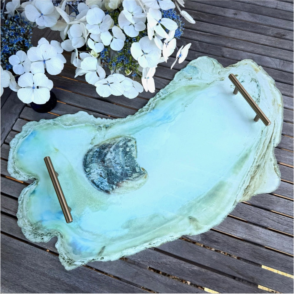 Large oyster shell with gold skewers on a wooden surface with white flowers in the background