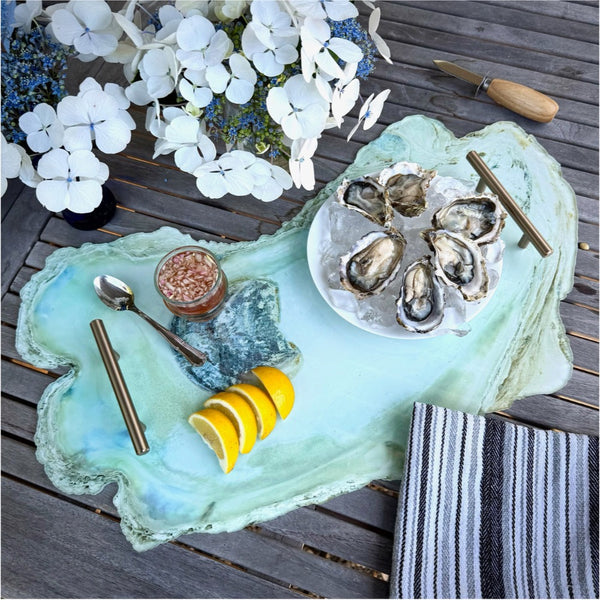 Oyster platter with oysters, lemon wedges, and a small jar on a decorative tray with flowers in the background.