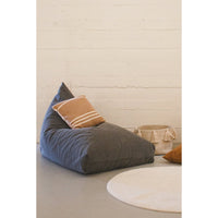 The Big Puff Emily Grey Floor Cushion by Lorena Canals with a brown pillow beside a basket and round beige rug.