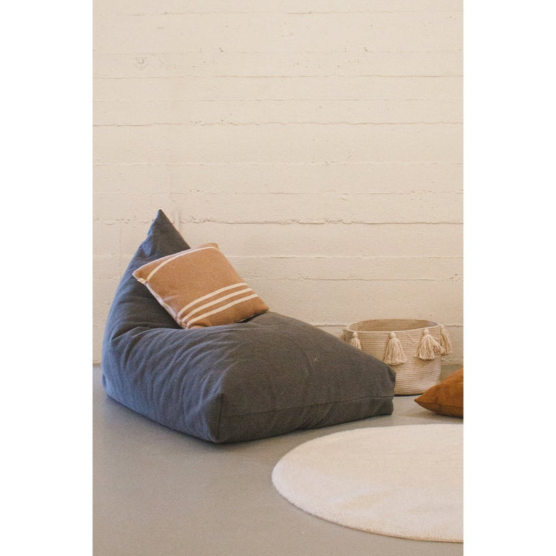 The Big Puff Emily Grey Floor Cushion by Lorena Canals with a brown pillow beside a basket and round beige rug.