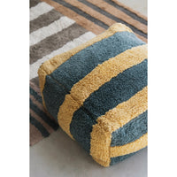 A square boucle pouf ottoman with alternating mustard yellow and slate blue-green stripes, shown on a striped area rug.