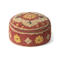 A round, low-profile tufted pouf or ottoman with a textured, looped pile. The design features a red base with yellow floral motifs, beige geometric borders, and small green accents, set against a plain white background.