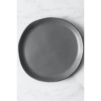 A dark gray ceramic plate with a matte finish and irregular hand-drawn edges, shown from a top-down perspective on a white marble surface.