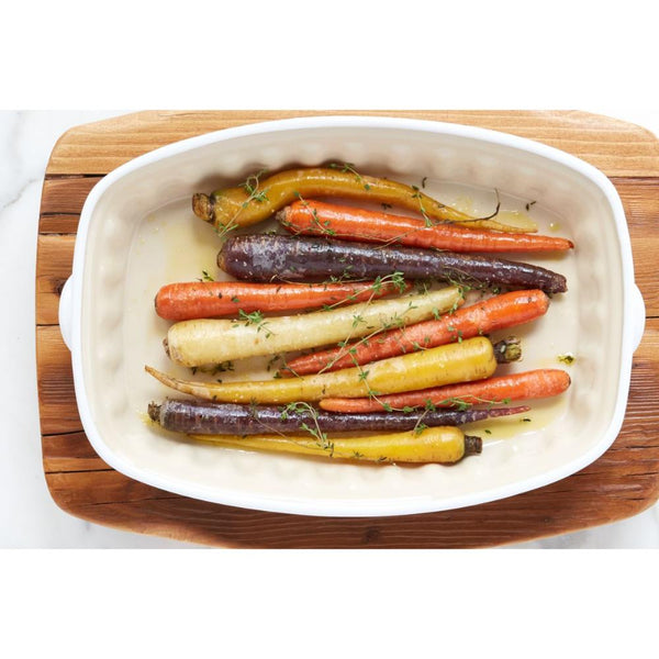 Roasted carrots in a white baking dish on a wooden cutting board