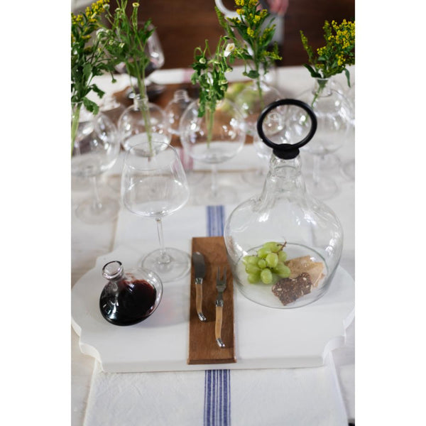 Dining table setting with wine glasses, cutlery, and small dishes on a white tablecloth.