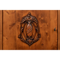 Close-up of a carved wooden cabinet door featuring an ornate oval crest inlaid into warm brown wood grain.