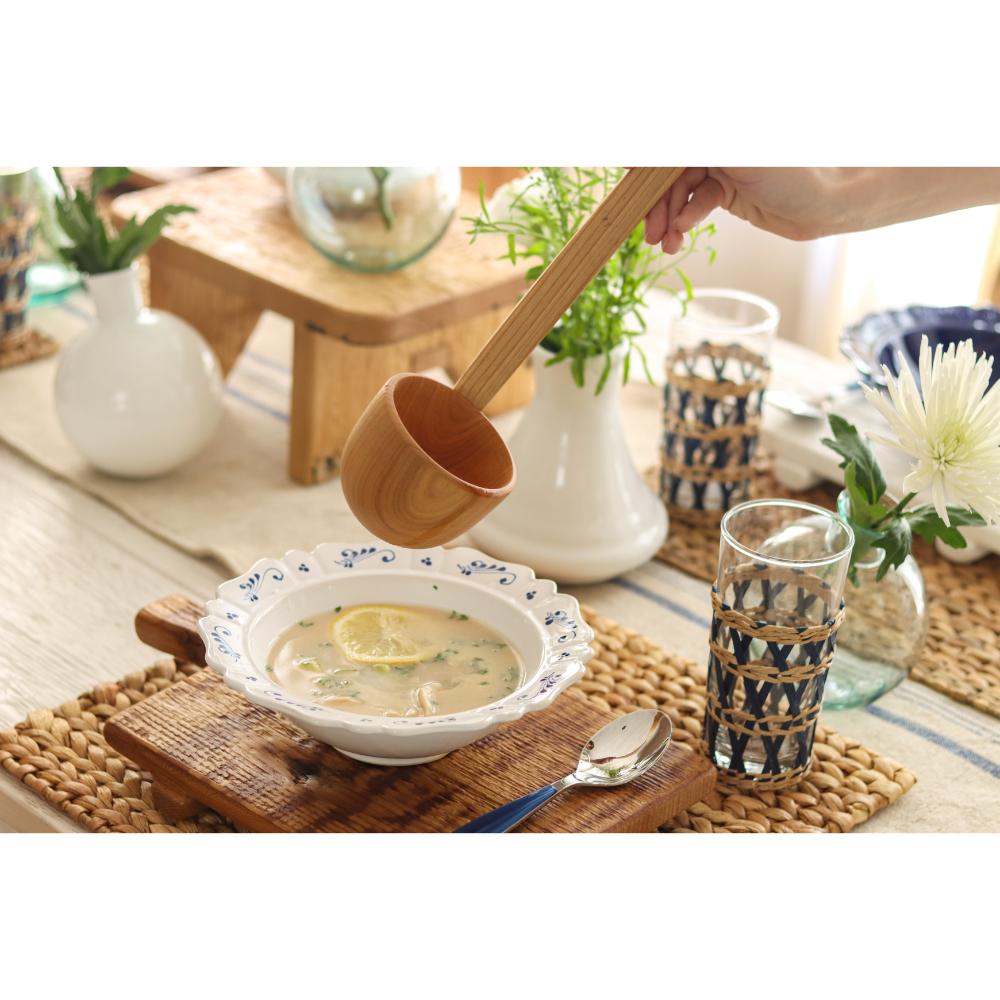 Bowl of soup with a wooden spoon, glass, and decorative items on a table.